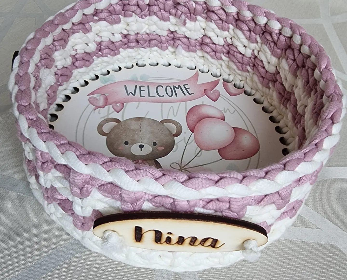Cestino a uncinetto in fettuccia rosa e bianca, fondo con orsetto, palloncini e scritta WELCOME, targhetta in legno Nina
